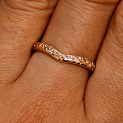 Close up view of a model's fingers wearing a 14k rose gold Curvy Chevron Diamond Stars Band