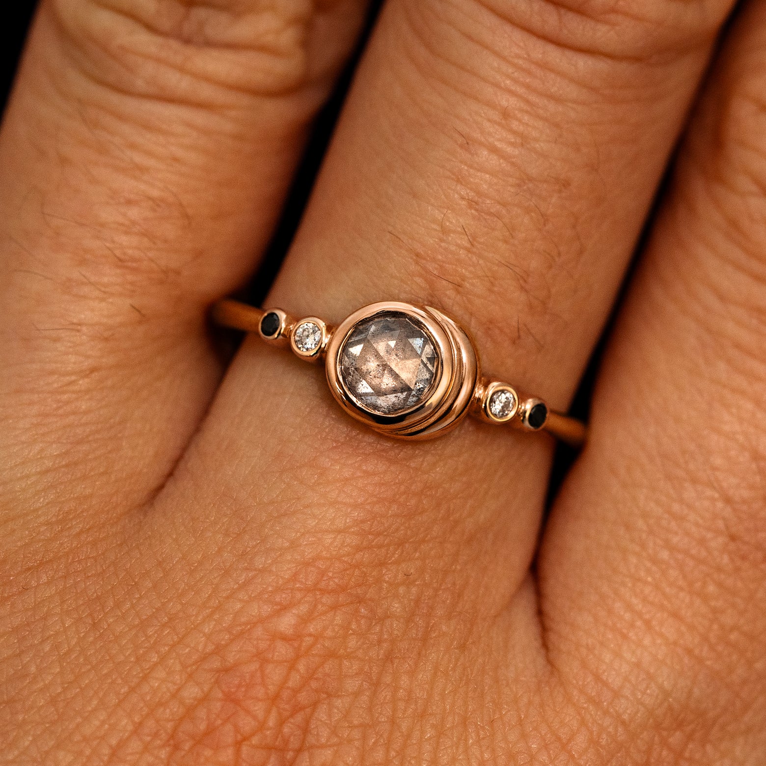 A model's hand wearing a 14k rose gold Rose Cut Salt and Pepper Diamond Moon Ring