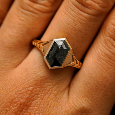 Close up view of a model's fingers wearing a 14k rose gold elongated hexagon black diamond engraved chronos ring