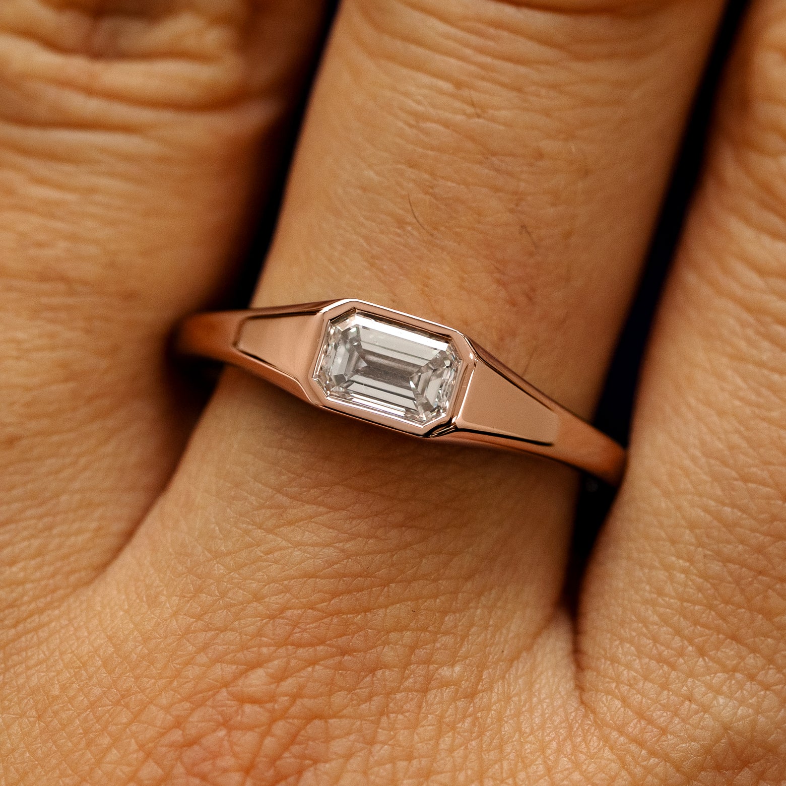 Close up view of a model's fingers wearing a 14k rose gold Emerald Cut Lab Created Diamond Signet Ring