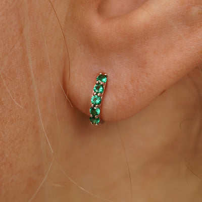 Close up view of a model's ear wearing a rose gold Small Emerald Huggie Hoop