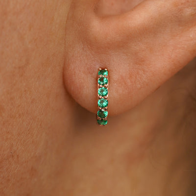 Close up view of a model's ear wearing a rose gold Small Emerald Huggie Hoop