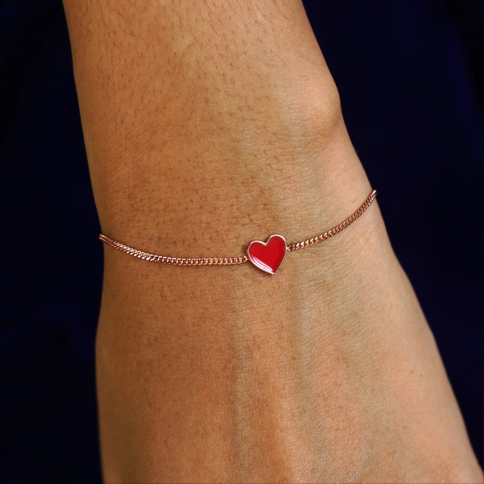 Close up view of a model's wrist wearing a rose gold red enamel heart bracelet