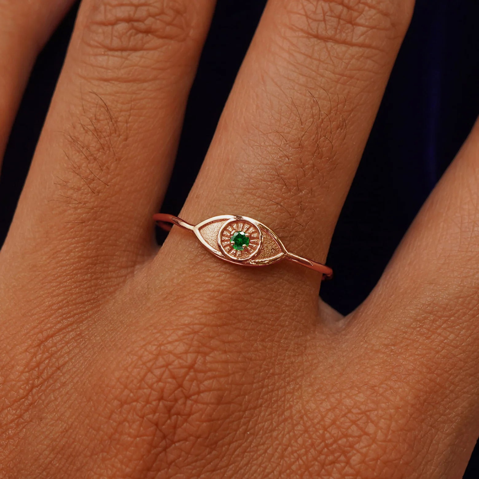 Close up view of a model's hand wearing a rose gold Evil Eye Ring in the Emerald gemstone option