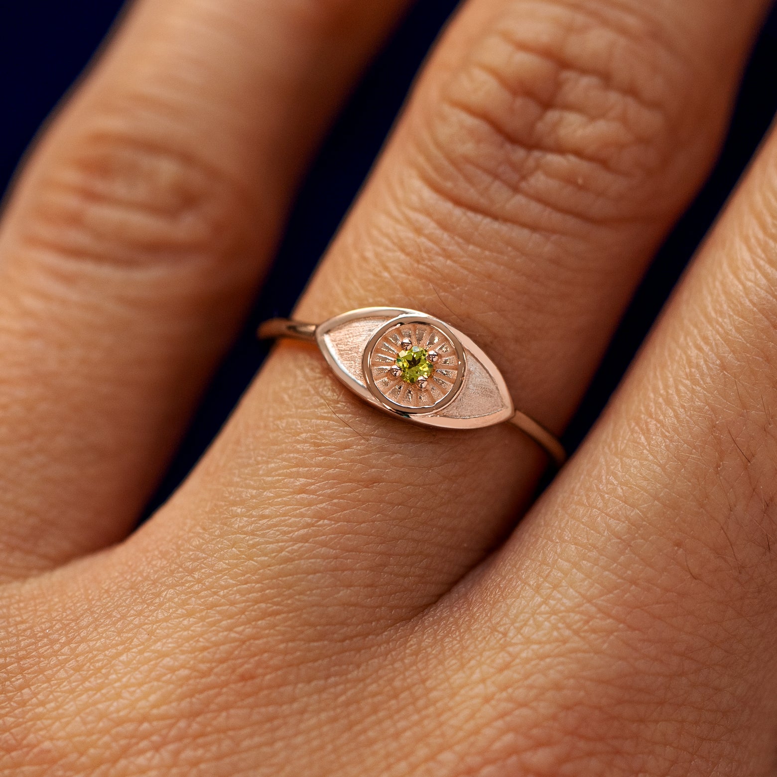 Close up view of a model's hand wearing a rose gold Evil Eye Ring in the Emerald gemstone option