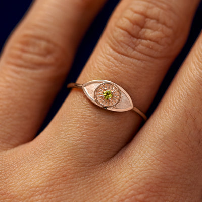 Close up view of a model's hand wearing a rose gold Evil Eye Ring in the Emerald gemstone option