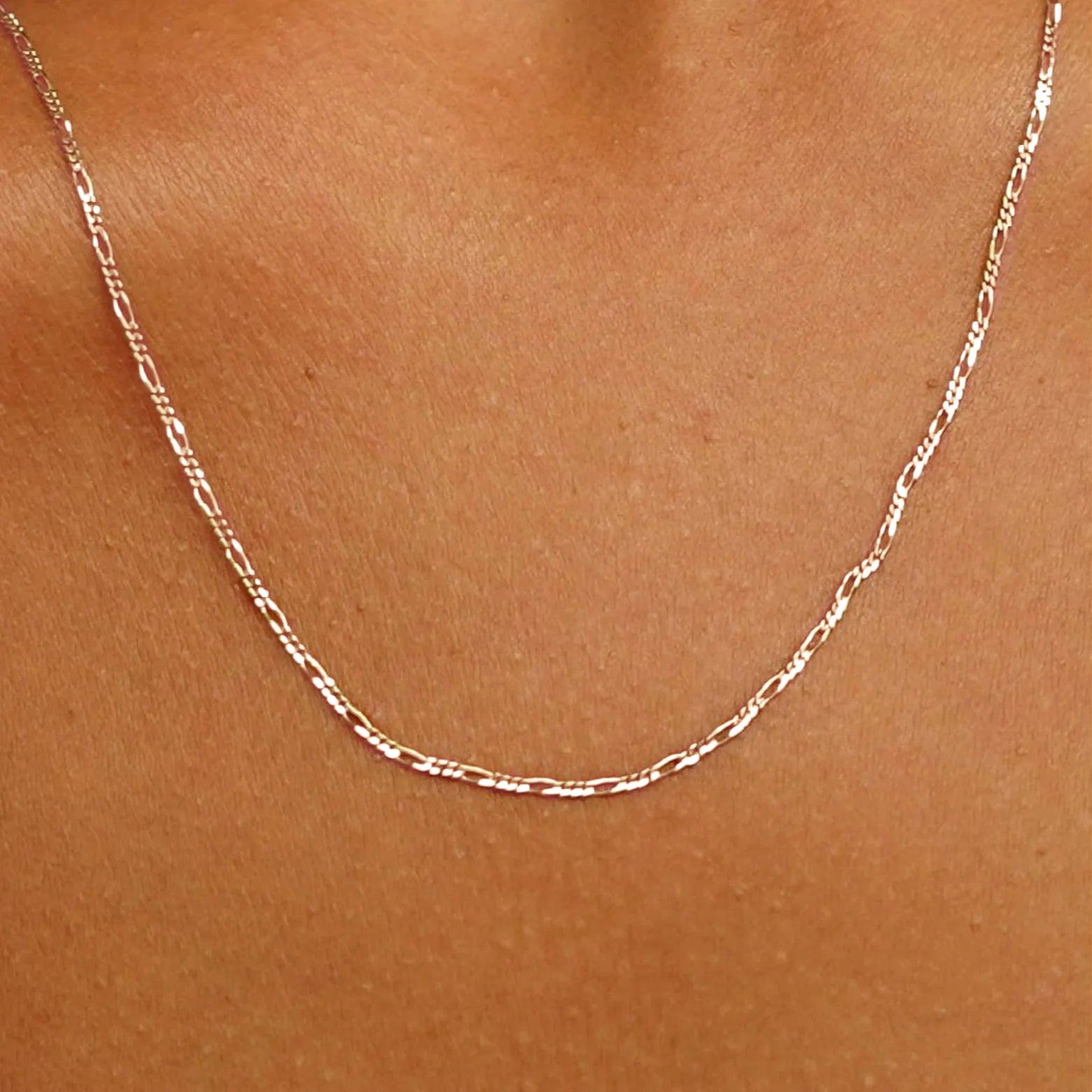 Close up view of a model's neck wearing a rose yellow gold Figaro Chain