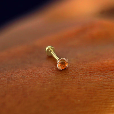 A solid 14k rose gold fire opal Piercing resting on the back of a model's hand