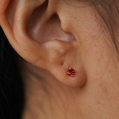 Close up view of a model's ear wearing a 14k rose gold Garnet Earring