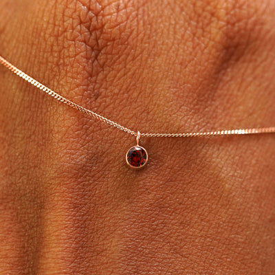 Close up view of a 14k rose gold Garnet Necklace draped across the back of a model's hand