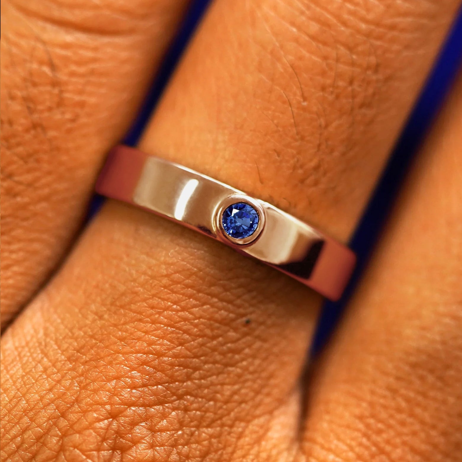 Close up view of a model's fingers wearing a 14k rose gold sapphire Gemstone Industrial Band