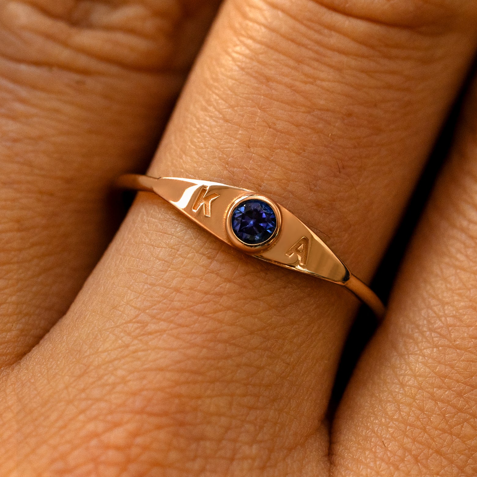 A model's finger wearing a sapphire champagne gold gemstone monogram ring with the initials K A