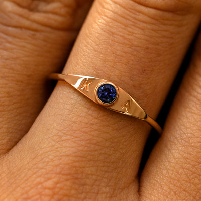 A model's finger wearing a sapphire champagne gold gemstone monogram ring with the initials K A