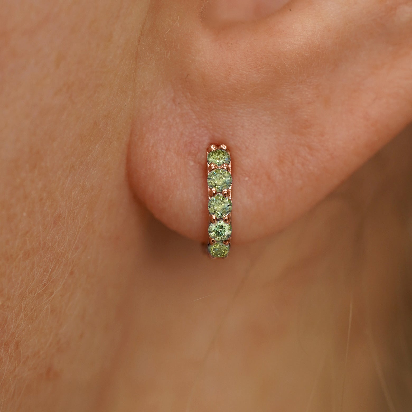 Close up view of a model's ear wearing a rose gold Mini Light Green Lab Diamond Huggie Hoop
