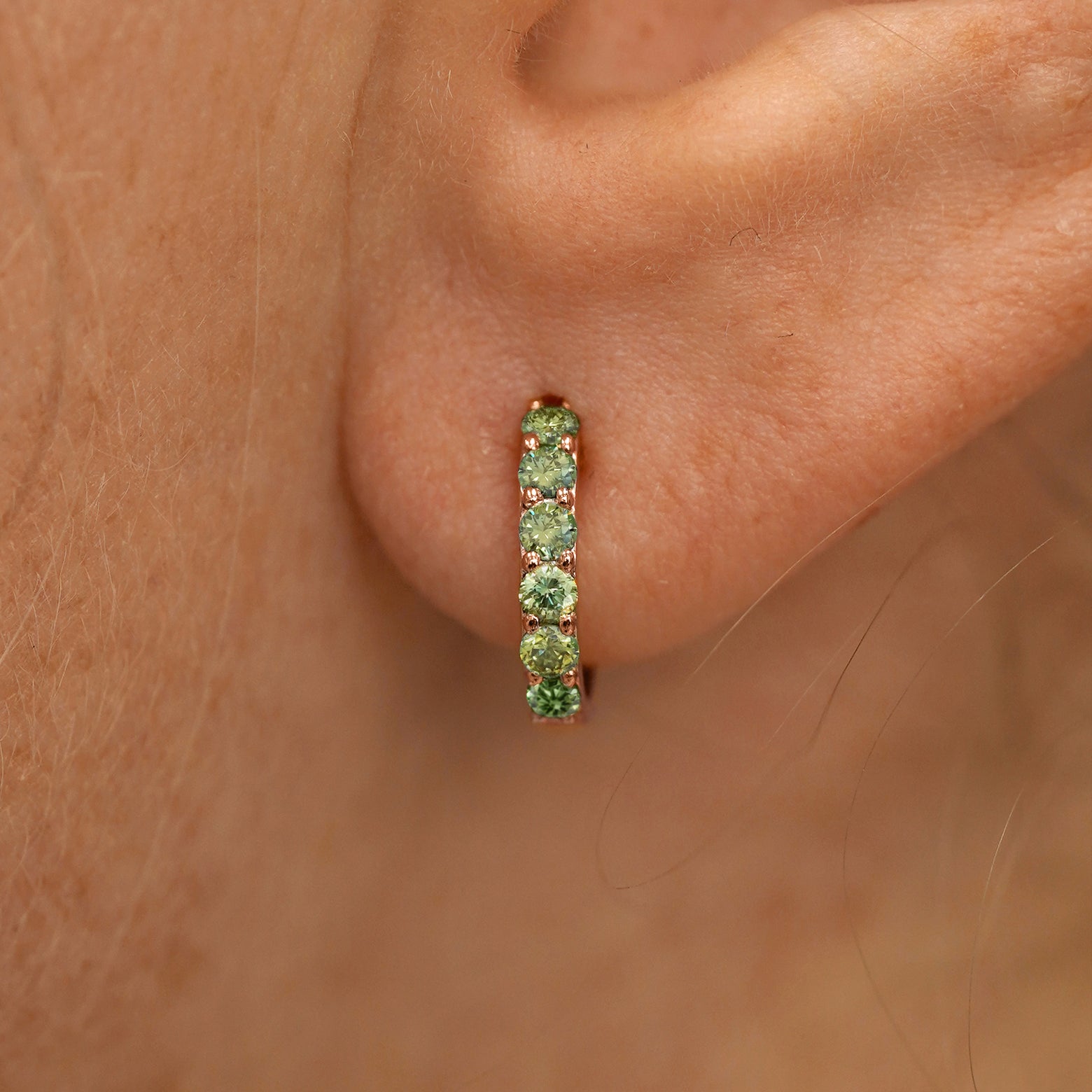 Close up view of a model's ear wearing a rose gold Small Light Green Lab Diamond Huggie Hoop