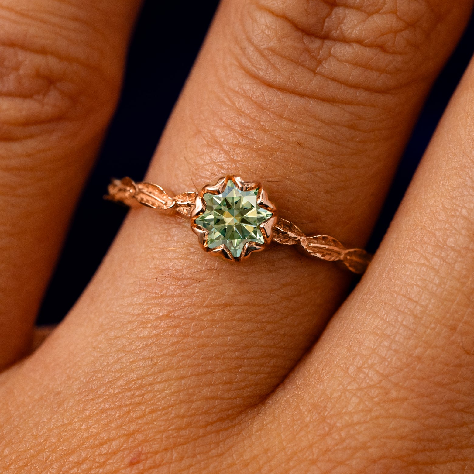 A solid 14k rose gold Green Moissanite Leaf Ring on a model's finger