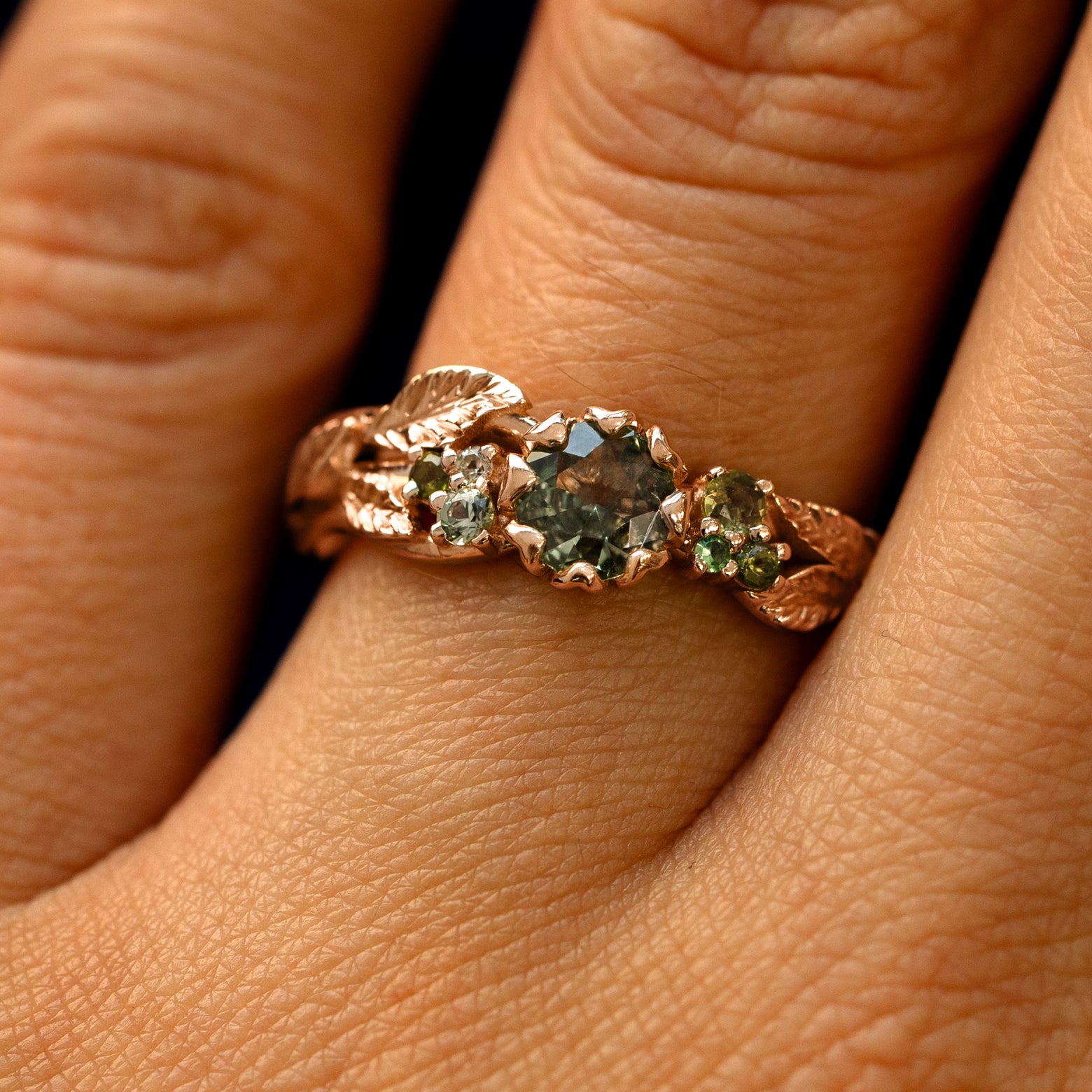 Close up view of a model's fingers wearing a 14k rose gold Green Sapphire Leaves and Vines Ring