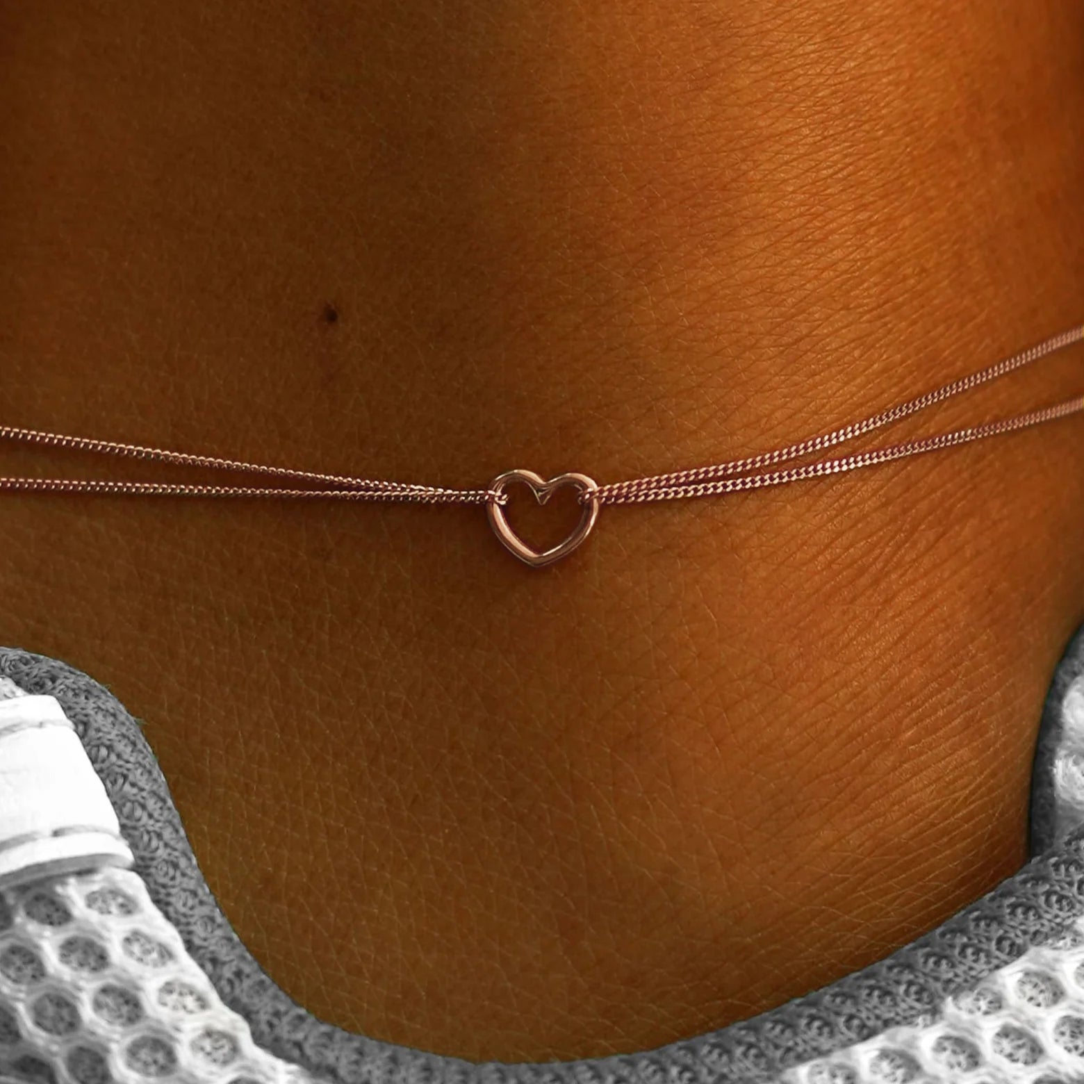 Close up view of a model's ankle wearing a 14k rose gold Heart Anklet