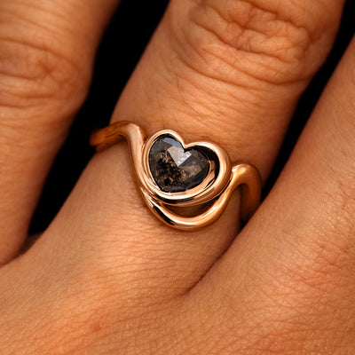A model's hand wearing a 14k rose gold Heart Salt and Pepper Diamond Infinite Wave Ring