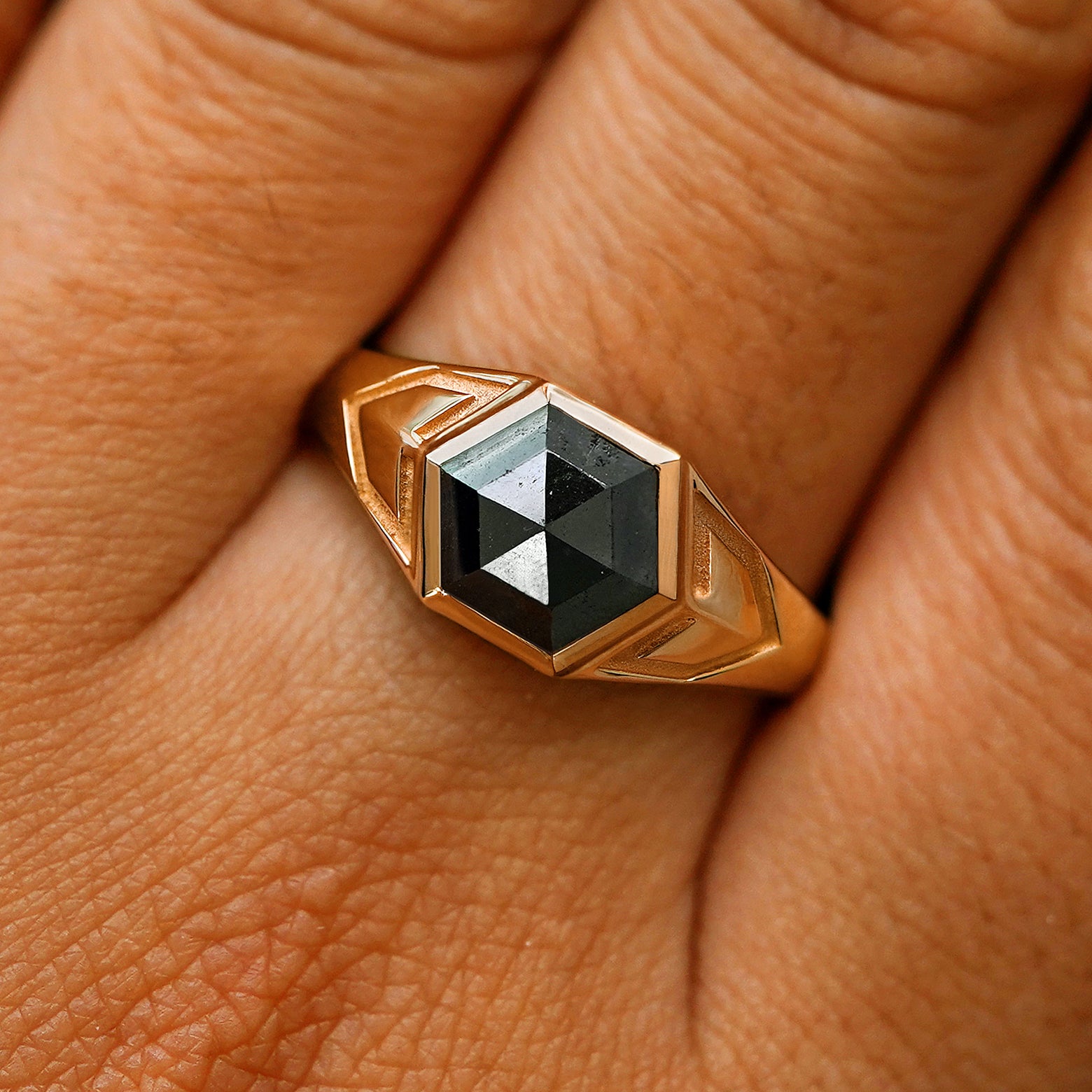 Close up view of a model's fingers wearing a 14k rose gold hexagon black diamond engraved transformation ring