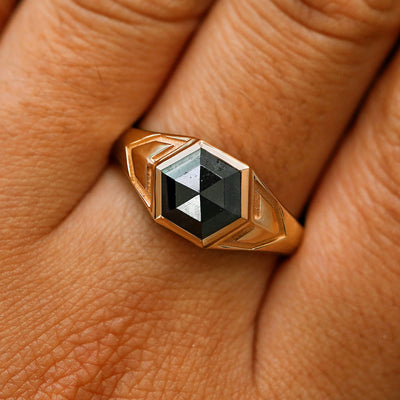 Close up view of a model's fingers wearing a 14k rose gold hexagon black diamond engraved transformation ring