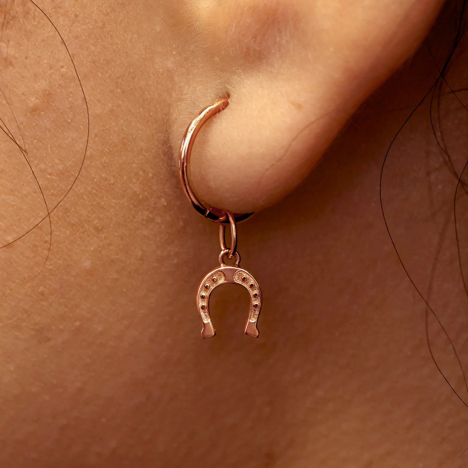 Close up view of a model's ear wearing a rose gold Horseshoe Charm on a Small Seamless Huggie Hoop