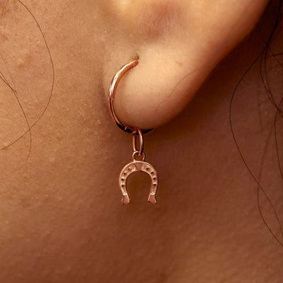 Close up view of a model's ear wearing a rose gold Horseshoe Charm on a Small Seamless Huggie Hoop