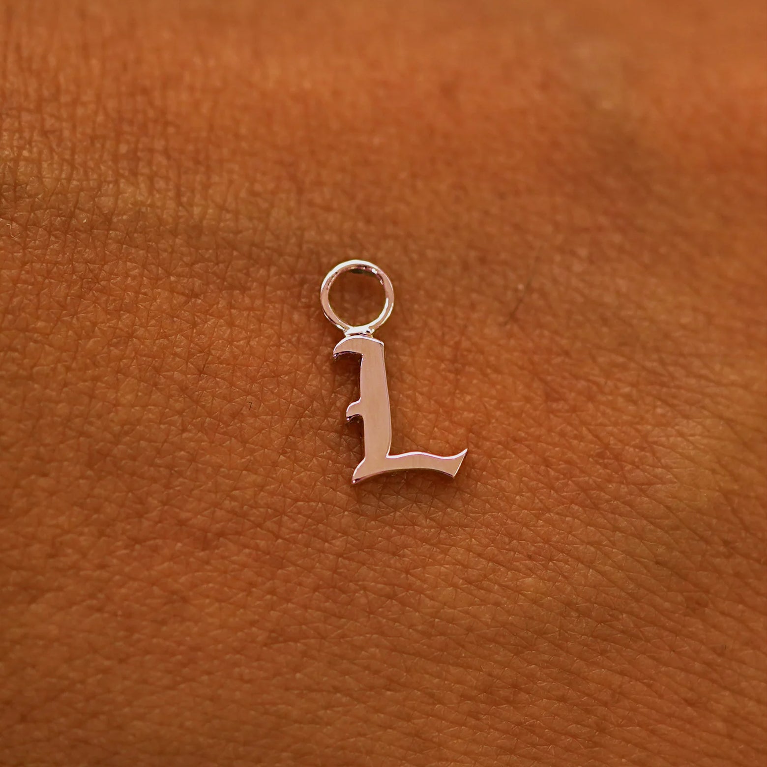 A solid 14k gold Initial Charm for earring in the letter L laying on the back of a model's hand