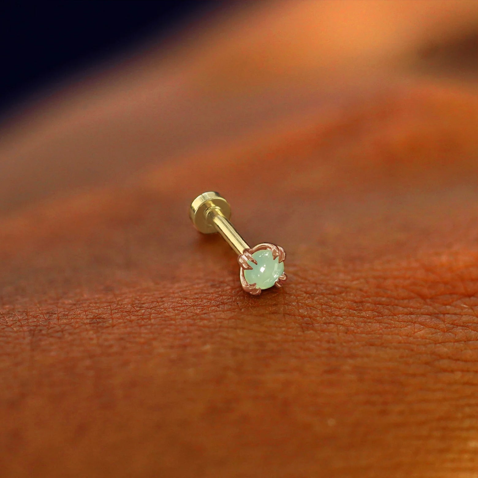 A solid 14k rose gold Jade Flatback Piercing resting on the back of a model's hand
