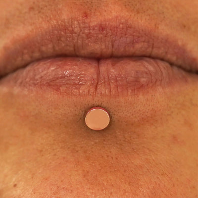 Close up view of a model's lips wearing a 14k rose gold Large Circle Flatback in a labret piercing