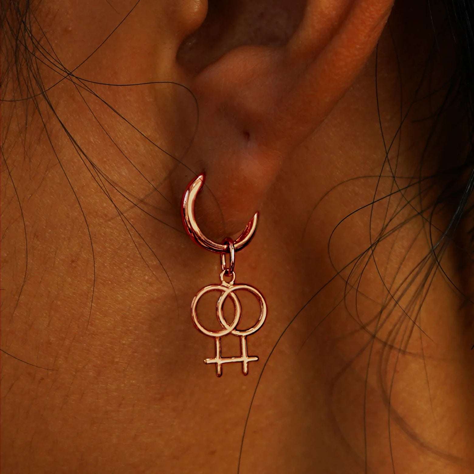 Close up view of a model's ear wearing a rose gold Lesbian Symbol Charm on a Curvy Huggie Hoop