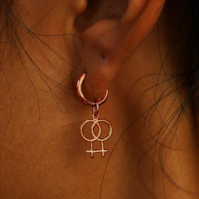 Close up view of a model's ear wearing a rose gold Lesbian Symbol Charm on a Curvy Huggie Hoop