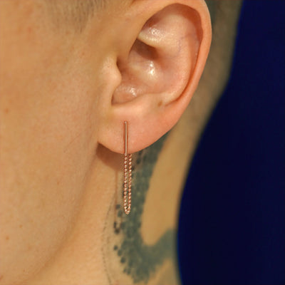 Close up view of a model's ear wearing a 14k rose gold Line Dangle Earring with the line vertical