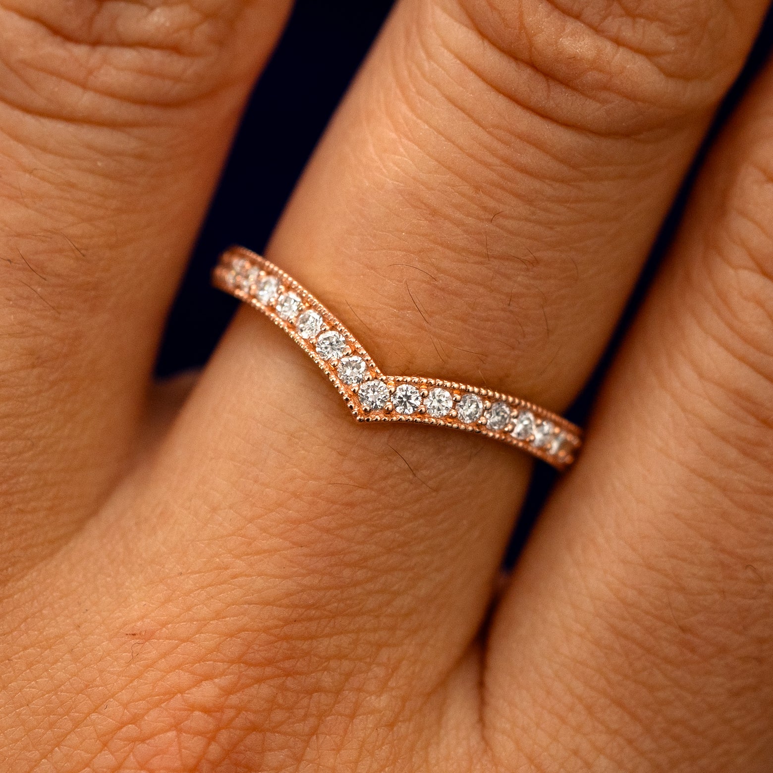 Close up view of a model's fingers wearing a 14k rose gold Milgrain Pave Diamond Chevron Band