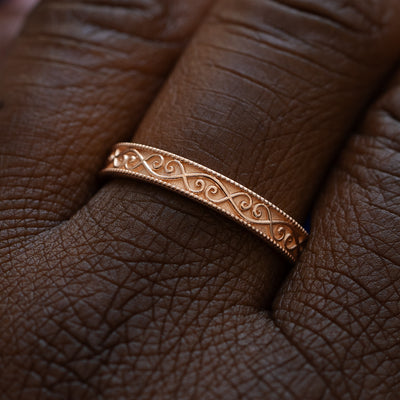Close up view of a model wearing a solid 14k rose gold milgrain scroll band
