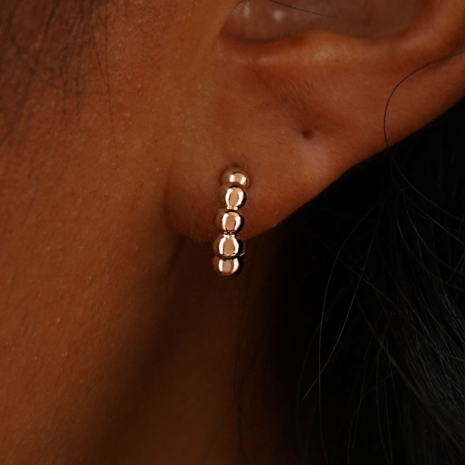 Close up view of a model's ear wearing a 14k rose gold Mini Puffy Beaded Hoop