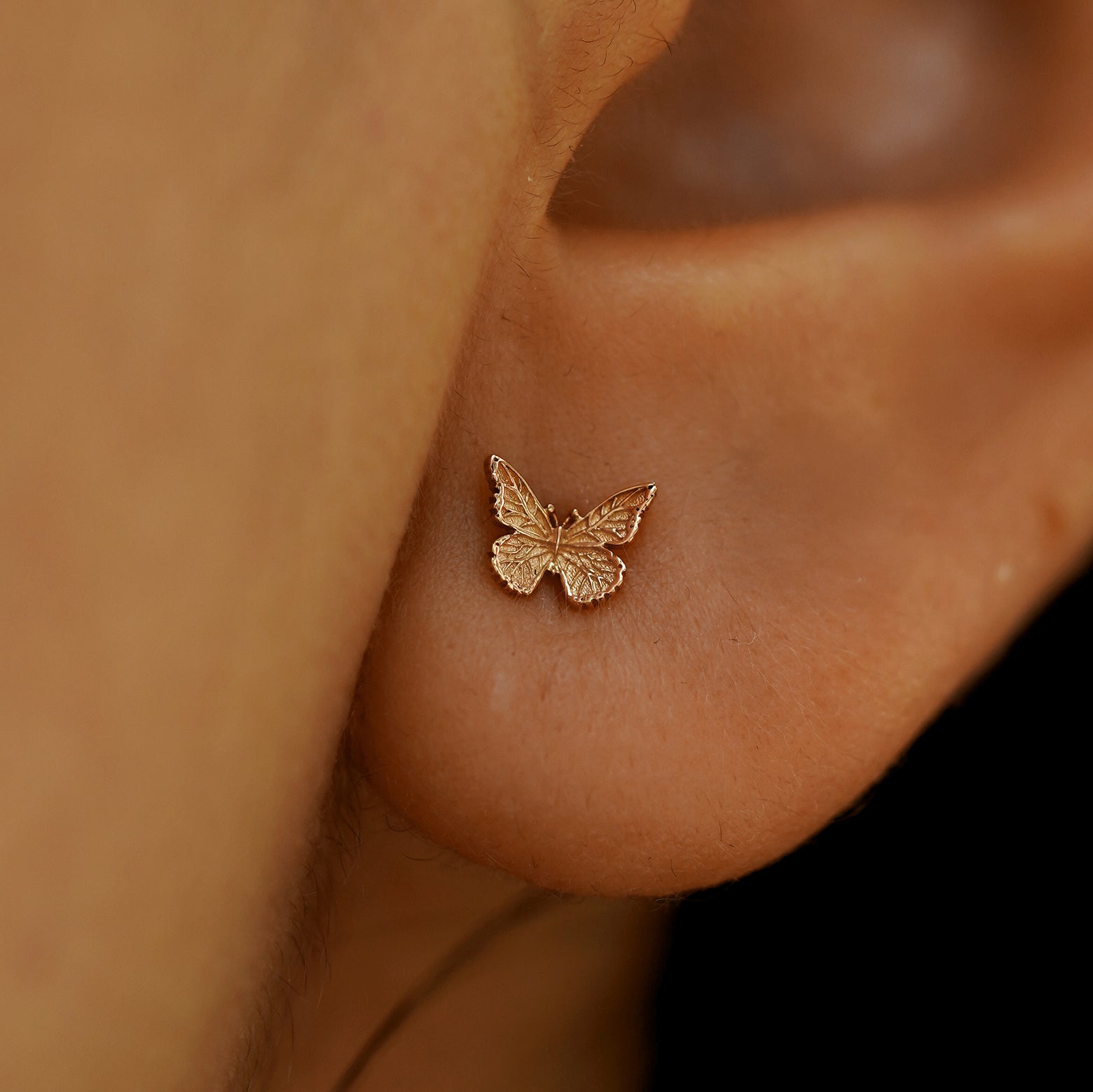 Close up view of a model's ear wearing a 14k rose gold Mini Butterfly Earring