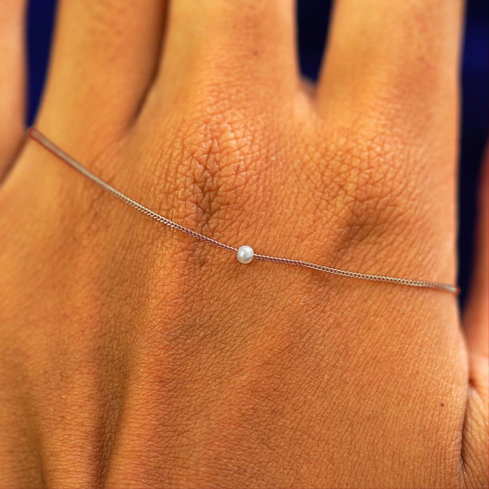 A rose gold 2mm pearl slide bracelet resting on the back of a model's hand