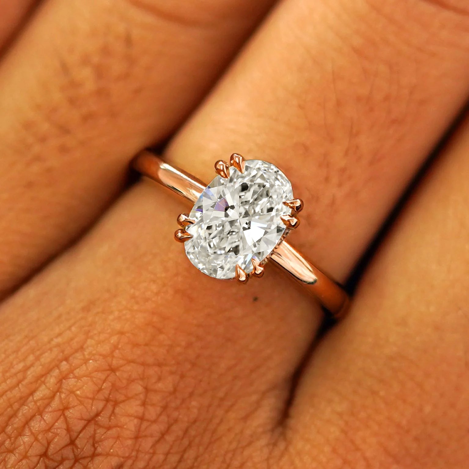 Close up view of a model's fingers wearing a 14k rose gold Oval Moissanite Halo Ring