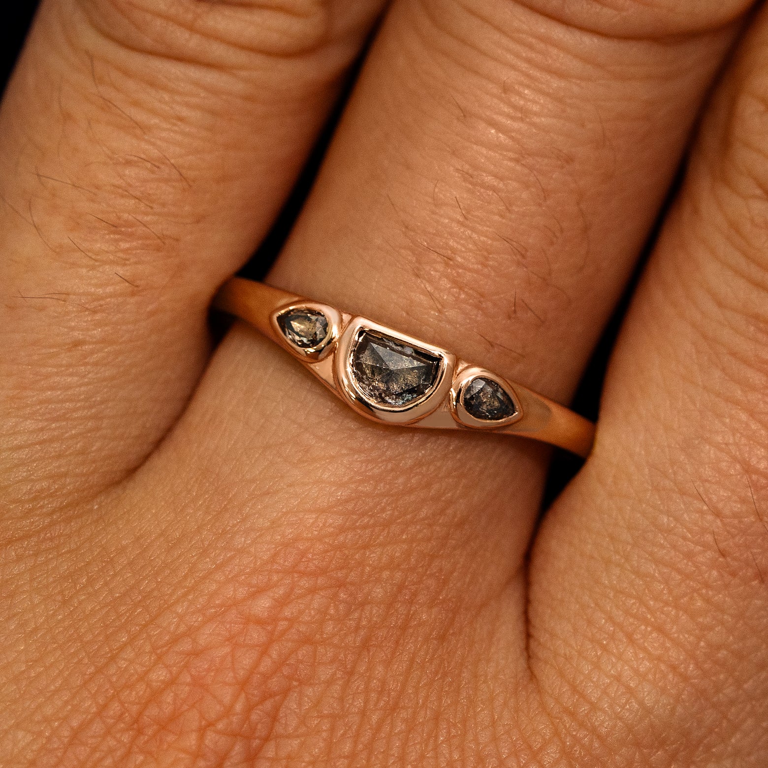 A model's hand wearing a 14k rose gold Moon Cut Salt and Pepper Diamond Ring