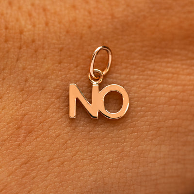 A solid 14k rose gold No Charm on the back of a models hand
