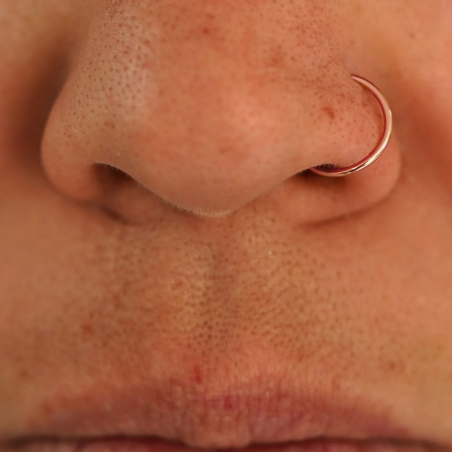 Close up view of a model's nose wearing a 14k rose gold Nose Ring Hoop