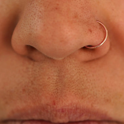 Close up view of a model's nose wearing a 14k rose gold Nose Ring Hoop
