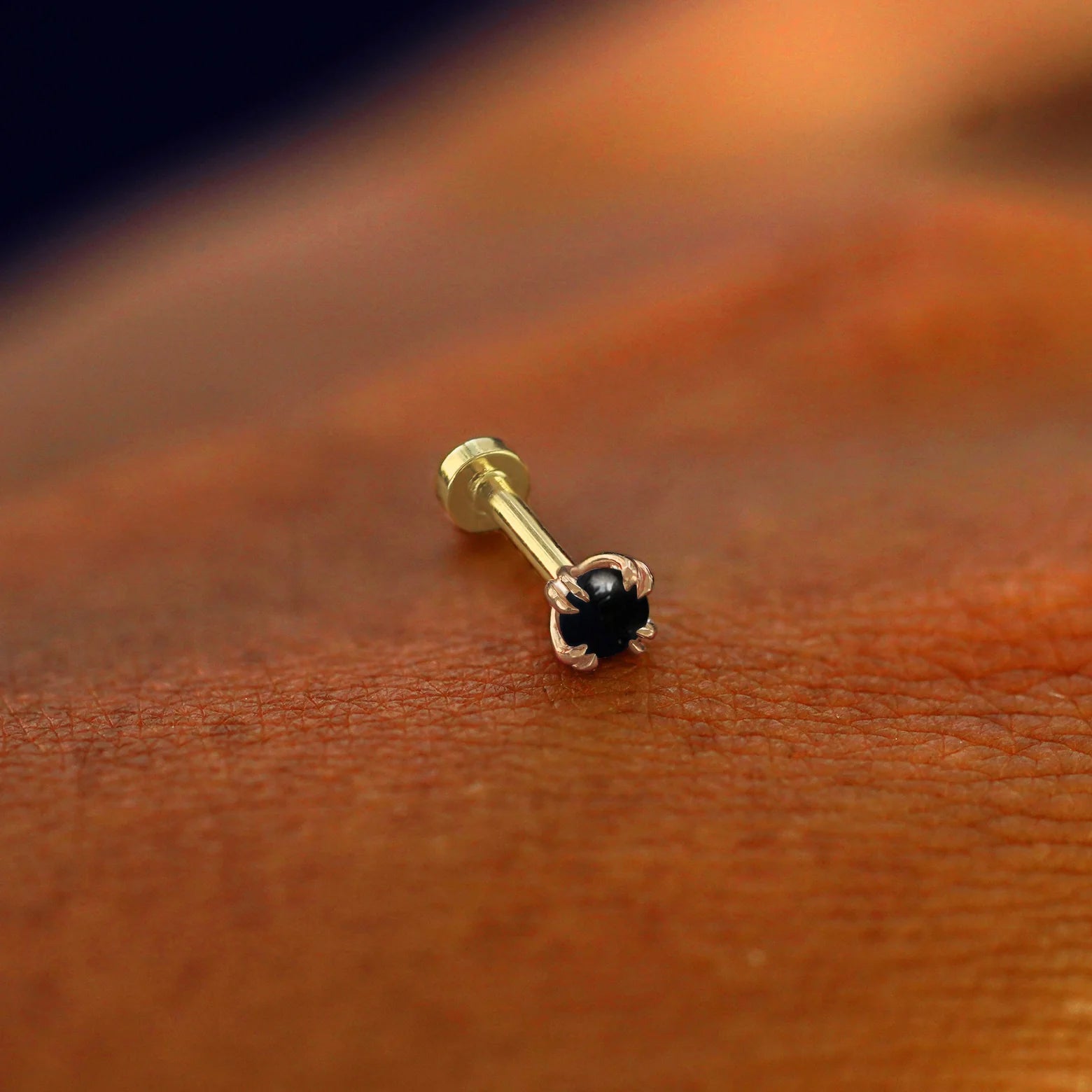 A solid 14k rose gold Onyx Flatback Piercing resting on the back of a model's hand