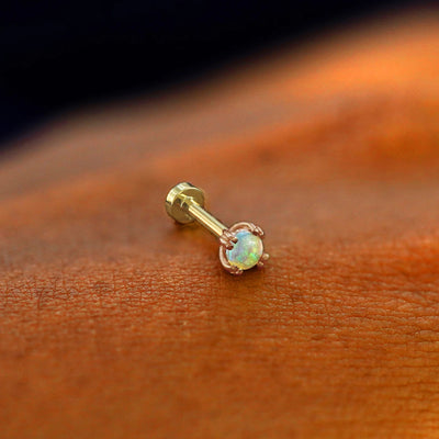 A solid 14k rose gold Opal Flatback Piercing resting on the back of a model's hand