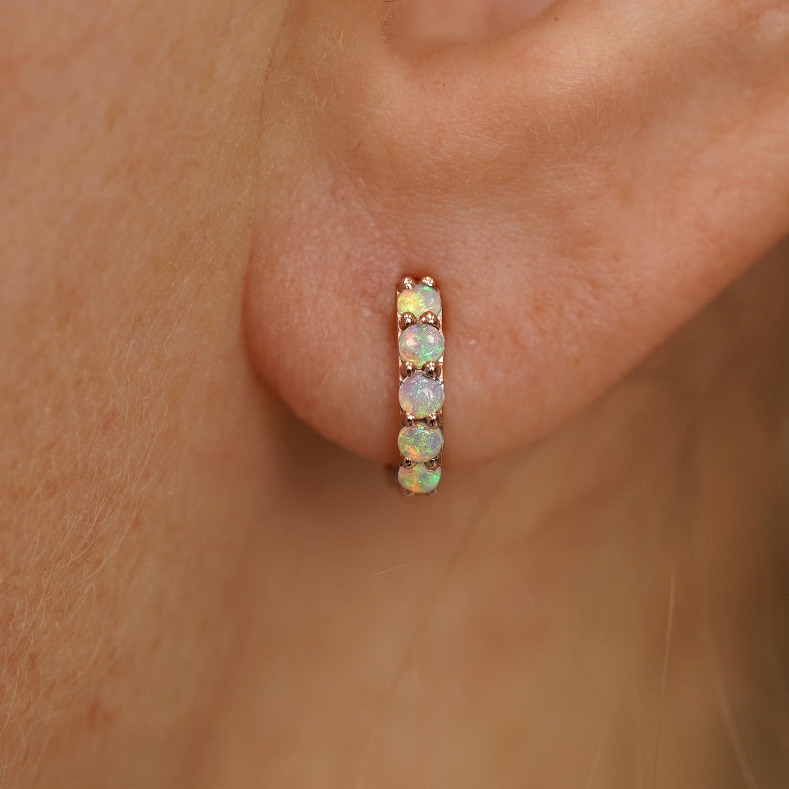 Close up view of a model's ear wearing a rose gold Mini Opal Huggie Hoop
