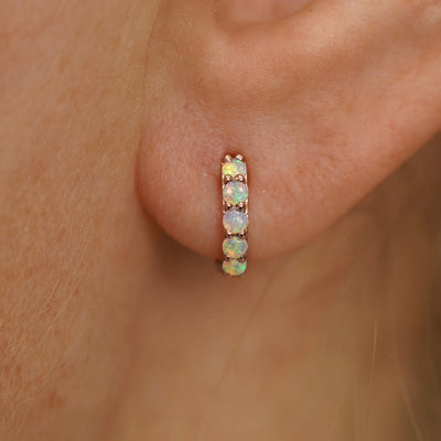 Close up view of a model's ear wearing a rose gold Mini Opal Huggie Hoop