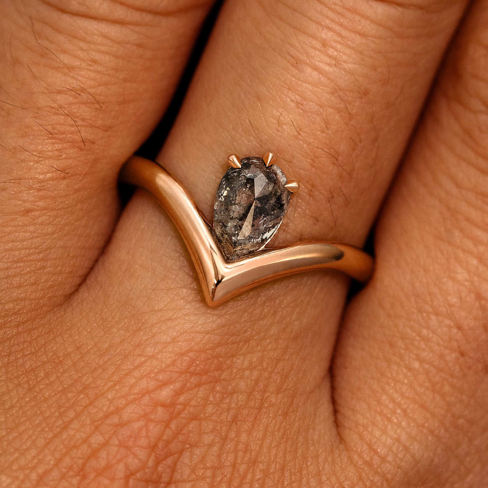 A model's hand wearing a 14k rose gold Pear Salt and Pepper Diamond Chevron Ring