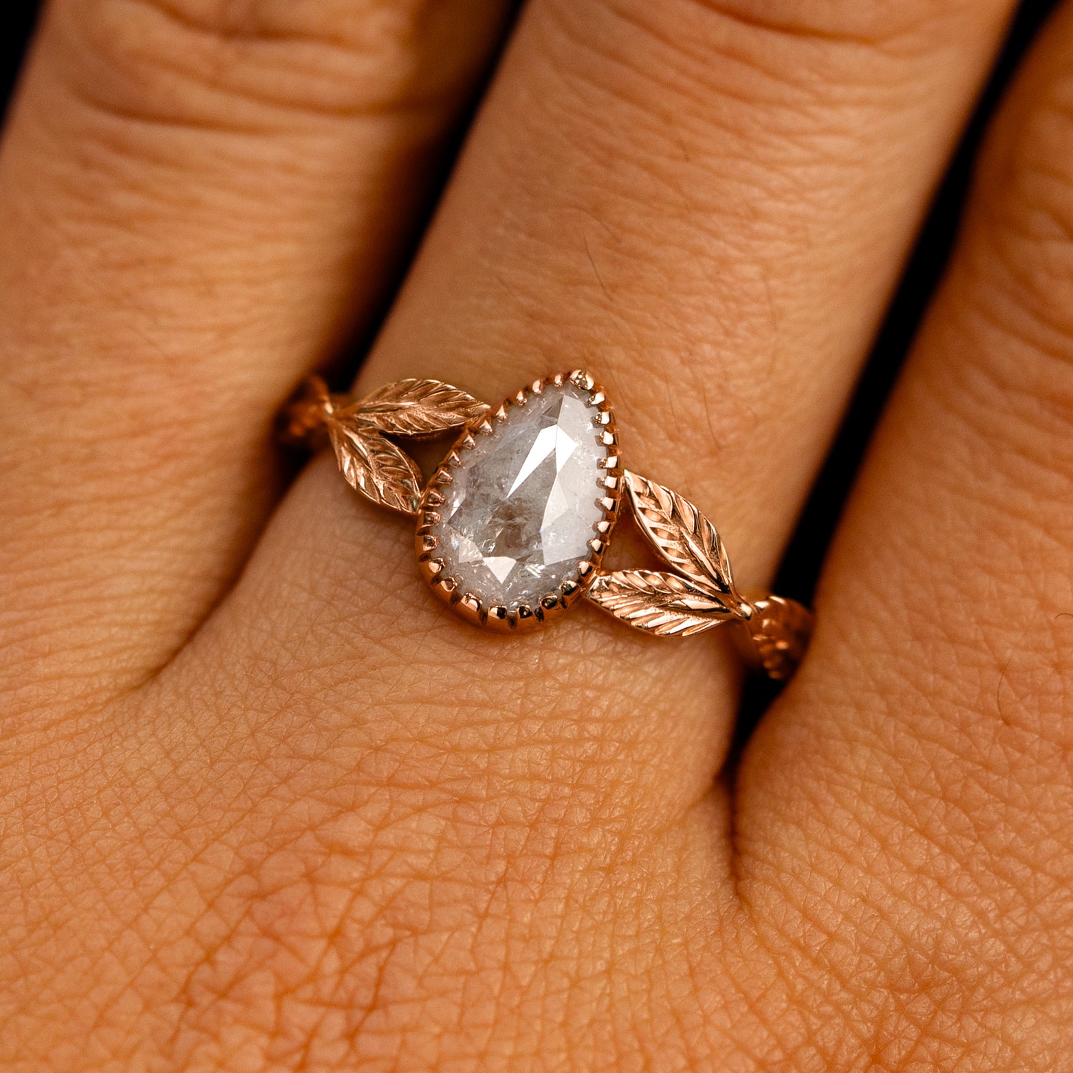 Close up view of a model's fingers wearing a 14k rose gold Pear Salt and Pepper Diamond Leaves Ring