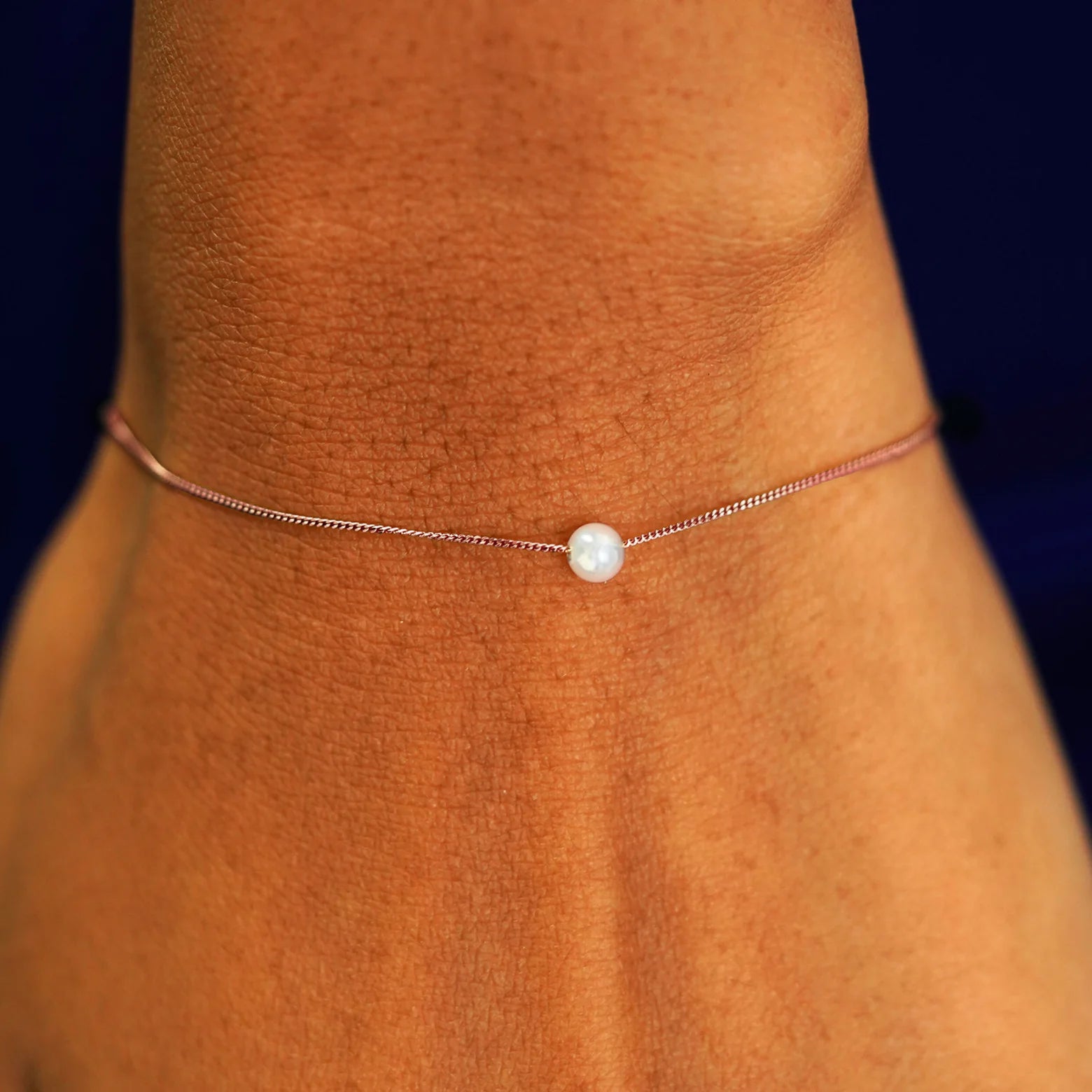 A model's wrist wearing a rose gold Pearl Slide Bracelet with a 4mm pearl
